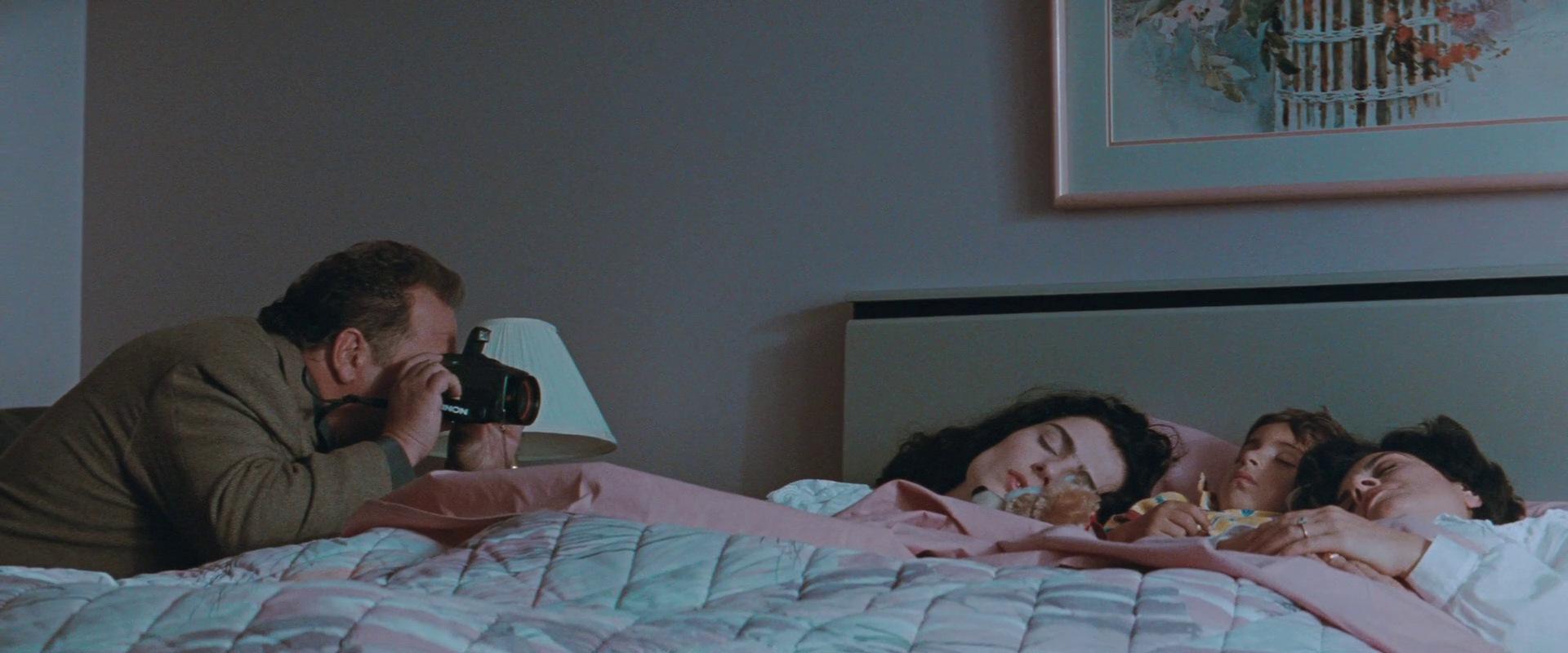 A man (L) takes a picture of two sleeping women in bed