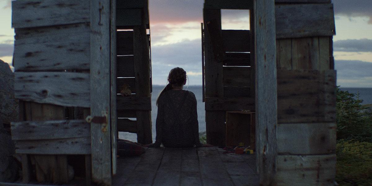 Isla (Alix West Lefler) sits with her back to the camera in a doorway