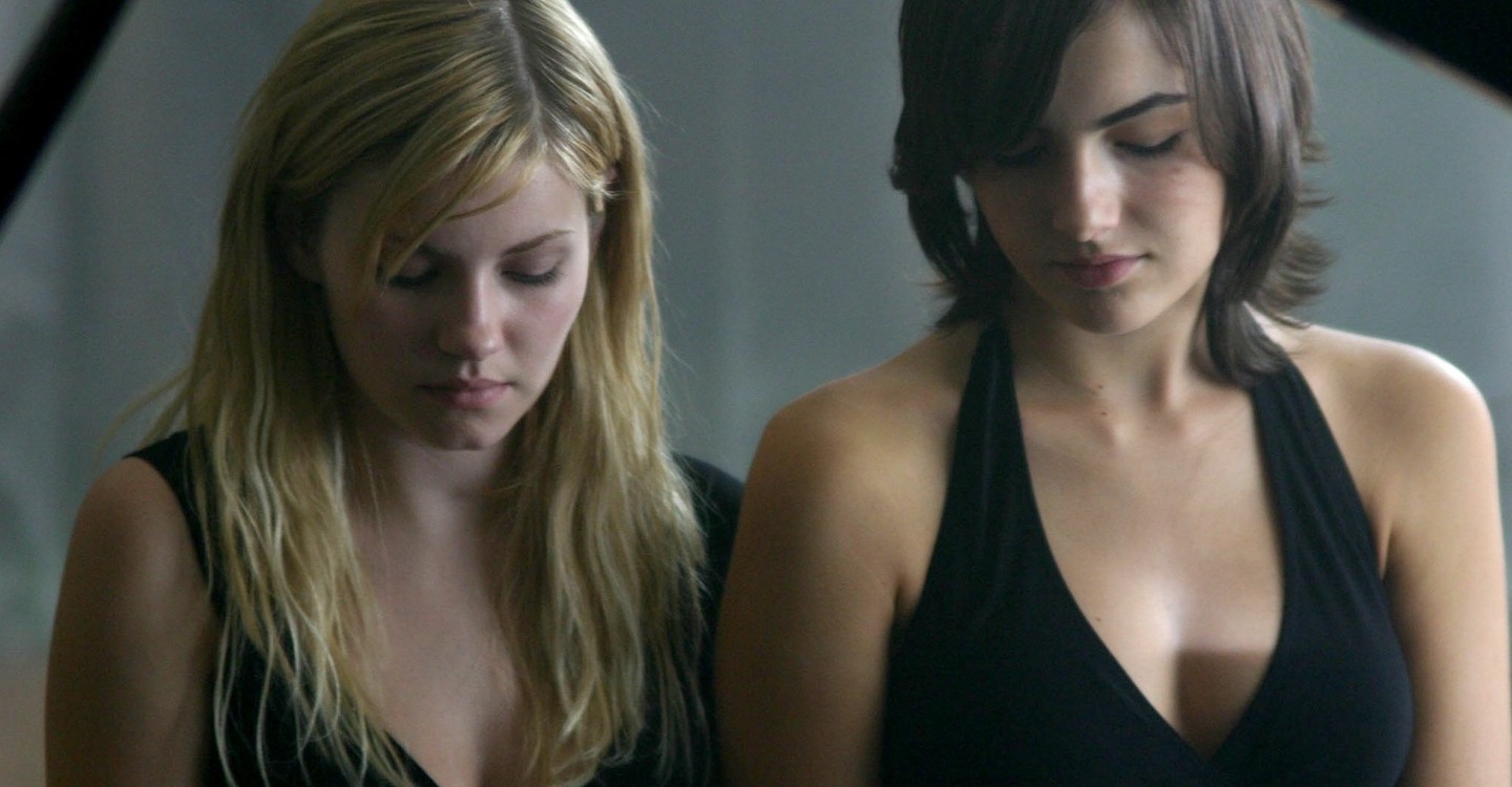 A blonde girl and a brunette sit at a piano