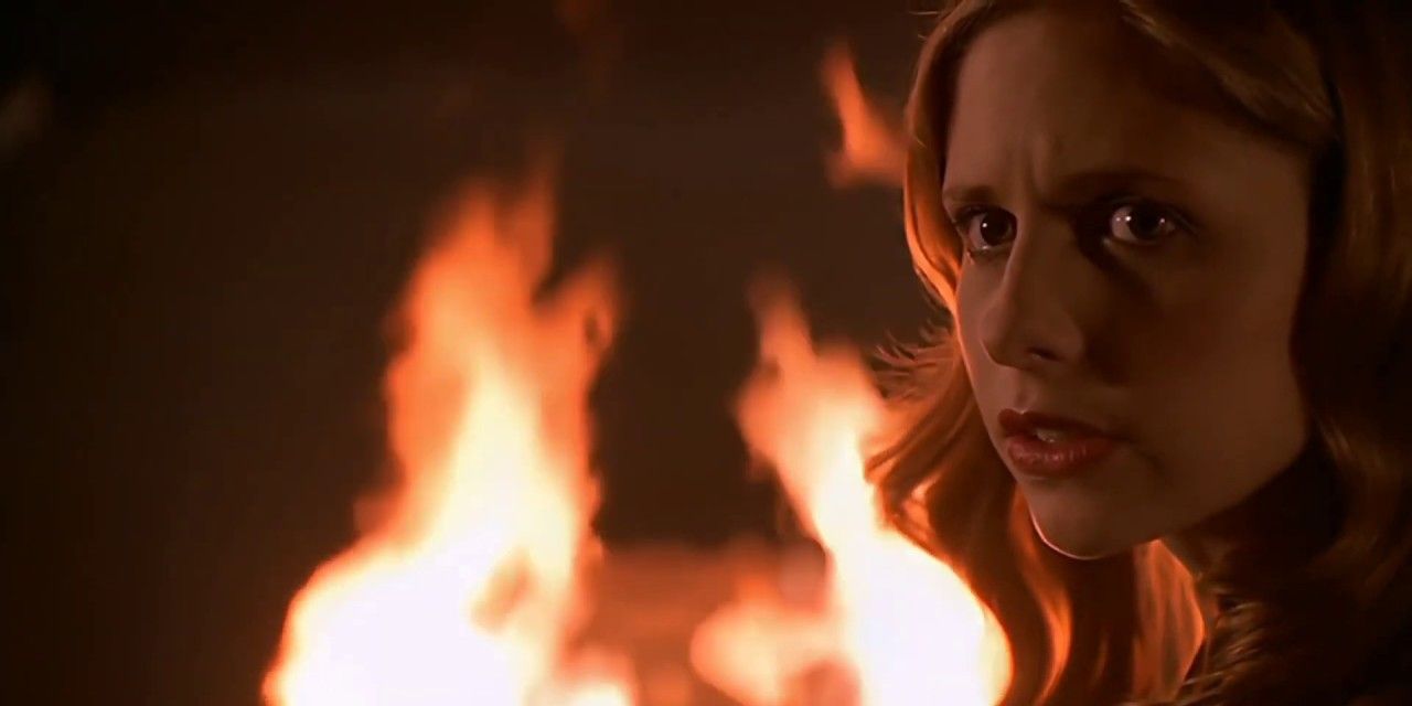 A blonde woman looks left while a fire rages behind her