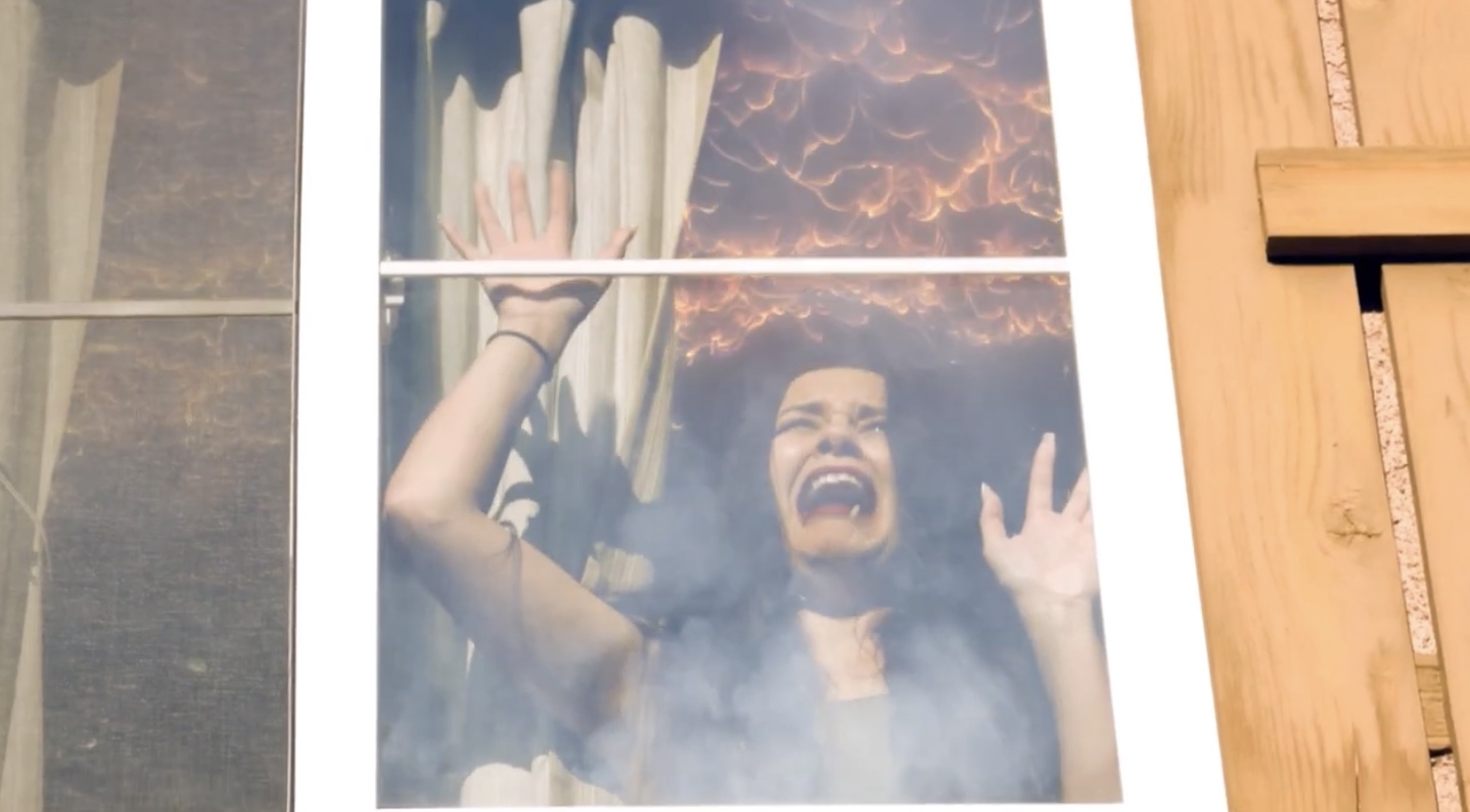 A screaming woman claws at the window in a fire lit room