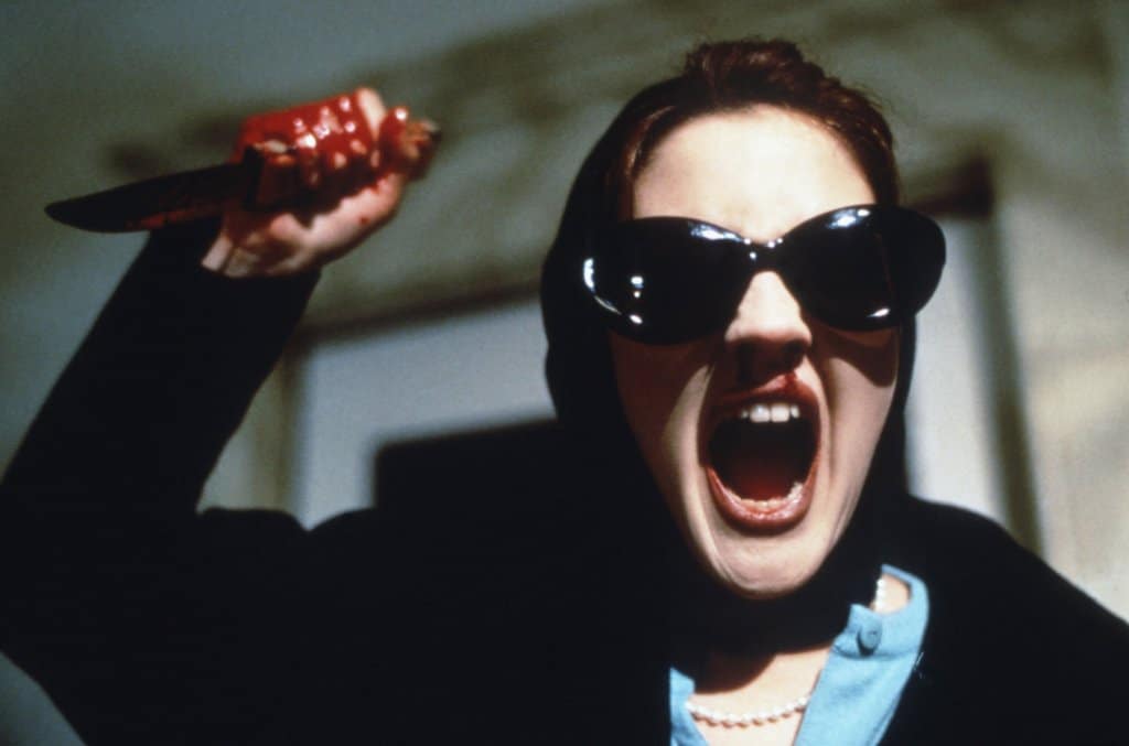 A woman in dark sunglasses and headscarf, screaming and wielding a pair of bloody scissors